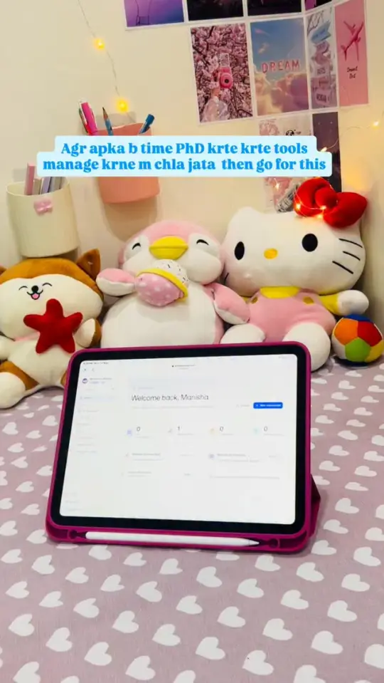 A tablet propped up on a desk showing an Alfred Scholar screen, with soft toys and a pinboard behind it